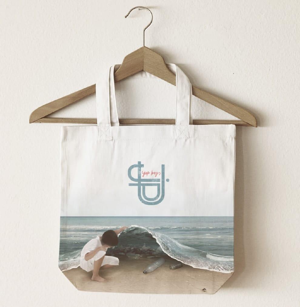 Canvas bag hanging from a wooden coathanger depicting a young girl holding up the ocean