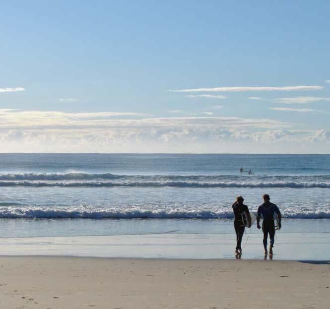 Man and Woman walking down a beach on a Summer's day about to go surfing