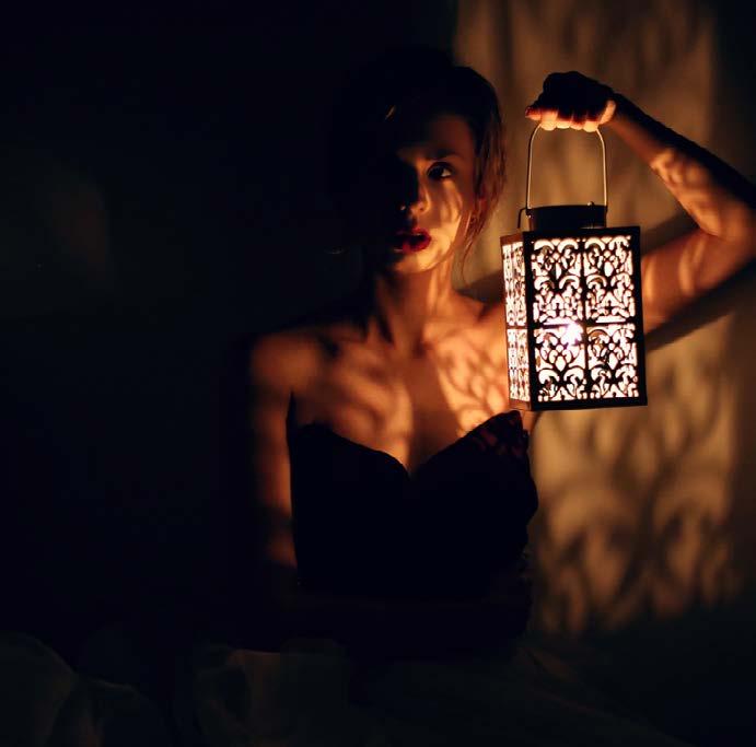 Woman in a black dress is holding an antique lamp in the dark looking lost